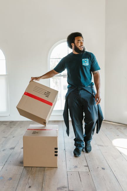 Two movers from Man with Van Shacklewell are engaged in a home relocation task, unloading a large piece of furniture wrapped in dark green protective cloth from the rear of a white moving van parked o