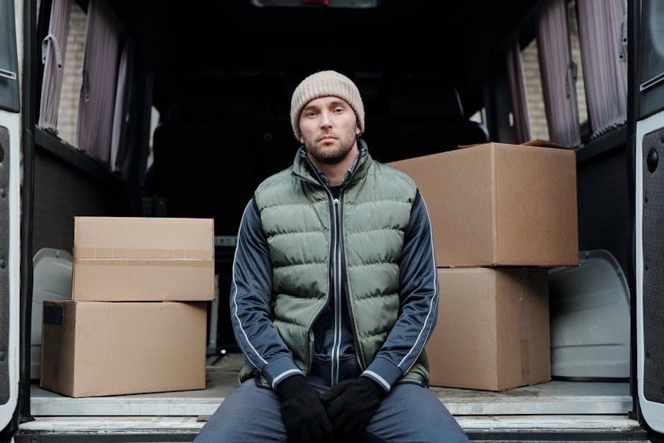 A man wearing casual clothing and a cap walking on the pavement beside a white panel van parked along a residential street in Shacklewell. The van is positioned next to a driveway, with a house featur