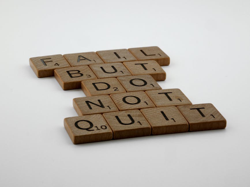 Close-up image of wooden Scrabble tiles spelling out the phrase 'FAIL BUT DO NOT QUIT' arranged on a plain white background. The tiles are evenly spaced and positioned in four rows, with each letter clearly visible and in uppercase. The image emphasizes the message of resilience and perseverance, which can relate to the challenges faced during house removals and the importance of proper planning and support in moving and relocation services. The neutral lighting highlights the natural wood grain of the tiles, reinforcing a professional and straightforward visual, suitable for content about home relocation and furniture transport, as provided by Man with Van Shacklewell.